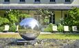 A round spherical water fountain with a house and sun loungers in the background