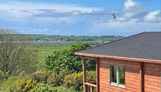 Blue sky with a swallow flying above the log cabin which looks out towards the sea.