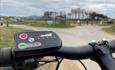 Close up photo of ebike handle with beach and forest in the distance.