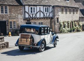 Vintage car driving past traditional cottages