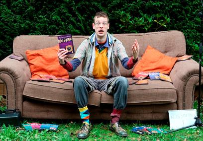 Man sitting on a sofa outdoors holding a DVD of the TV show Friends