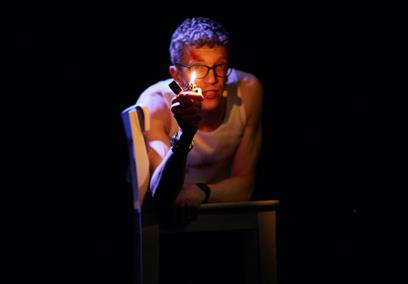 A man holding a lighter while leaning on a chair in a dark room