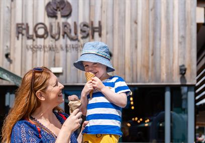 A woman with a child sitting on her shoulder. Both are eating ice creams.