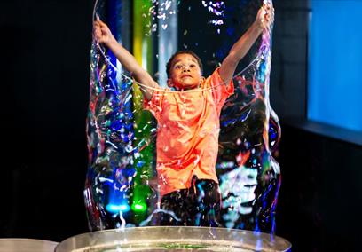 A small boy wearing an orange t shirt creating a large bubble