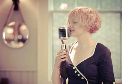 A blonde lady wearing a black dress singing into a microphone