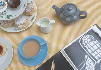 A cream tea set up with a sketchbook in the corner
