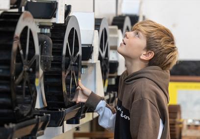 Boy looking at some large cogs on a machine at Saltford Brass Mill