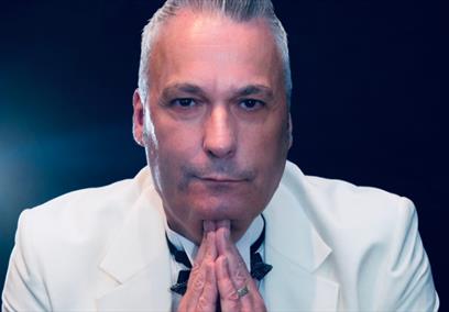 An older man wearing a white tux holing his head up with his hands