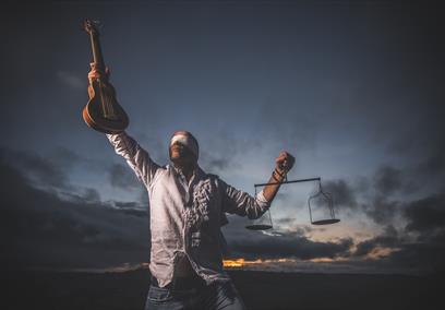 A blindfolded man carrying the scales of justice and a guitar