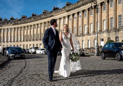A bride and groom holding hands and walking along the Royal Crescent in Bath