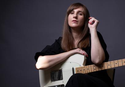 A woman posing with a guitar on her lap