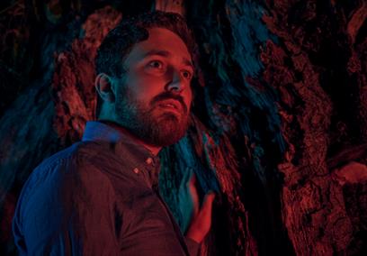 Man holding tree looking into distance with dark red light
