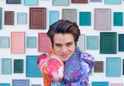Jim Fishwick in front of a white wall covered in colourful tiles