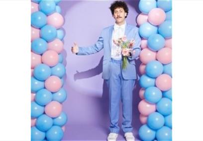 Schalk Bezuidenhout in a purple suit in front of a balloon arch