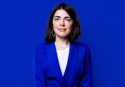 Rosie Holt in a blue suit sat infront of a blue background