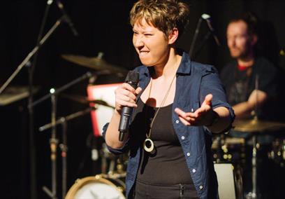 A female wearing a black tank top and blue overshirt performing on stage