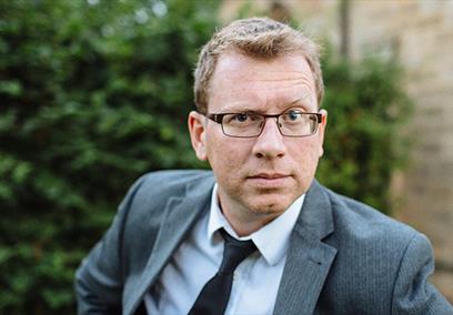 Man with glasses looking into camera with one eyebrow raised