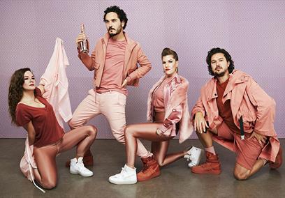 4 peole wearing all pink outfits infront of a purple backdrop