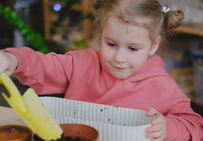 A child wearing a pink jumper holding a yellow shovel digging in mud