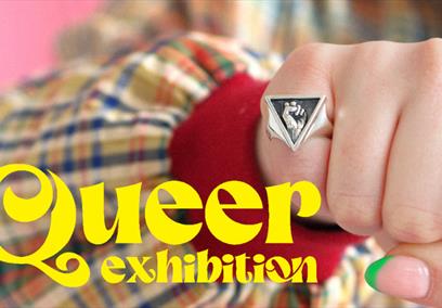 A picture of a fist with a ring and the words 'Queer Exhibition' overlaid in yellow text