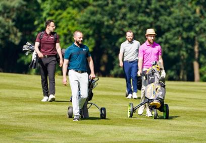 A group of 4 men wheeling gold caddies on a golf course