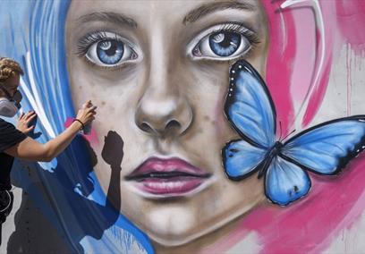 Person spraying mural of girl's face with butterfly