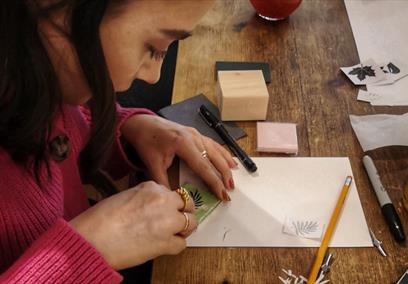 A female wearing a pink jumper carving a stamp