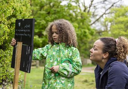 A child and parent looking at a trail sign in a garden.