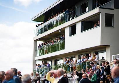 A crowd of spectators watching from the stands at Bath Racecourse