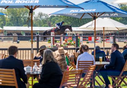 Royal Windsor Horse Show - people at tables under parasols watching showjumping