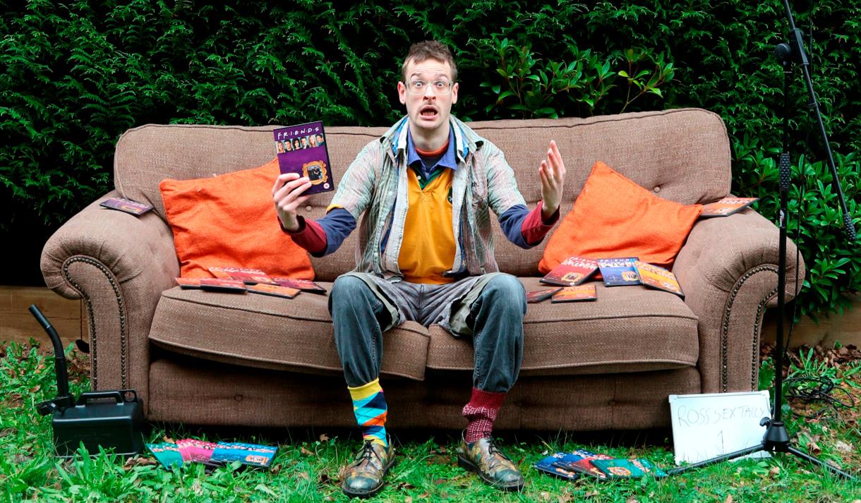 Man sitting on a sofa outdoors holding a DVD of the TV show Friends