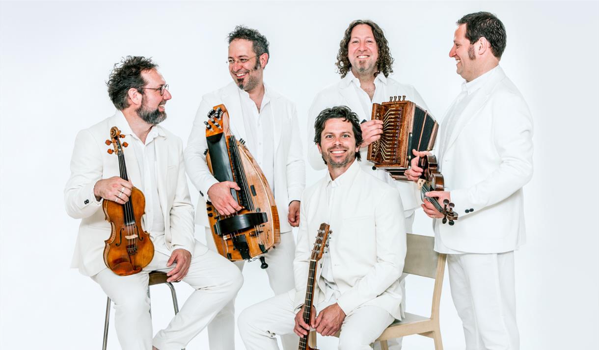 An image of five men in white suits holding instruments