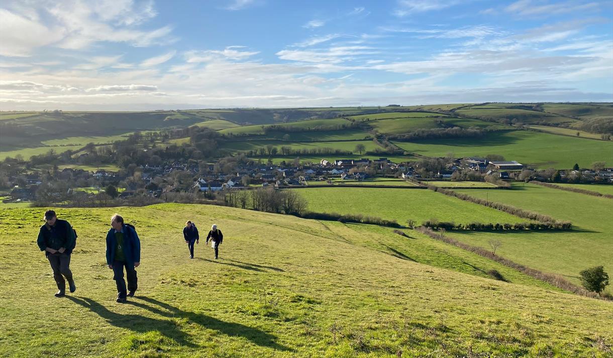 A walking group hiking over a field with a village view in background
