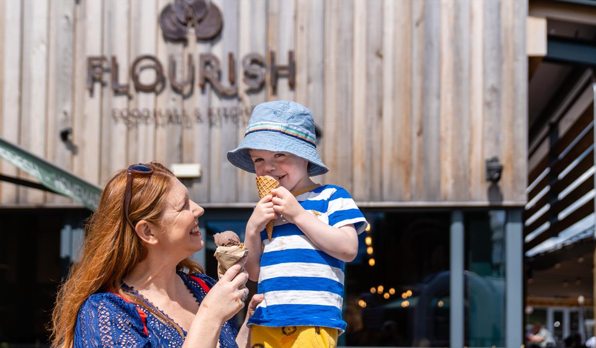 A woman with a child sitting on her shoulder. Both are eating ice creams.