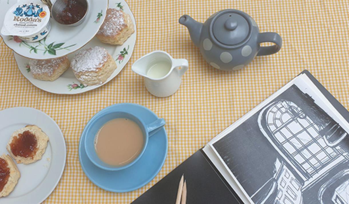 A cream tea set up with a sketchbook in the corner