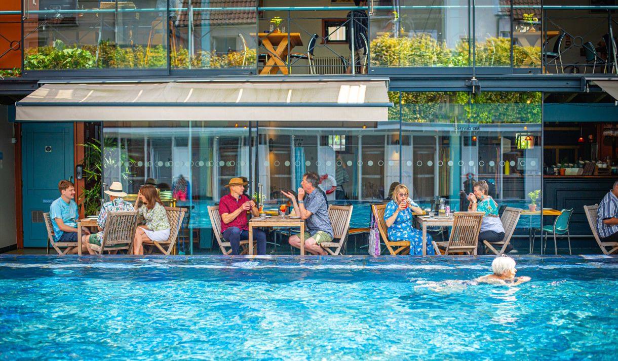 Bristol Lido - person swimming in pool and people dining by restaurant