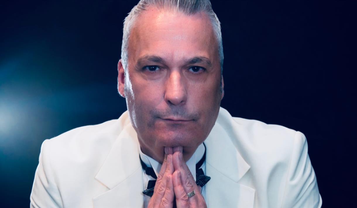 An older man wearing a white tux holing his head up with his hands