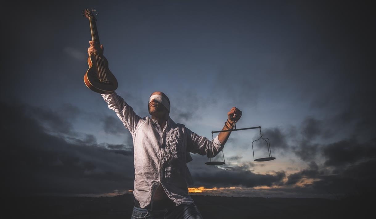 A blindfolded man carrying the scales of justice and a guitar
