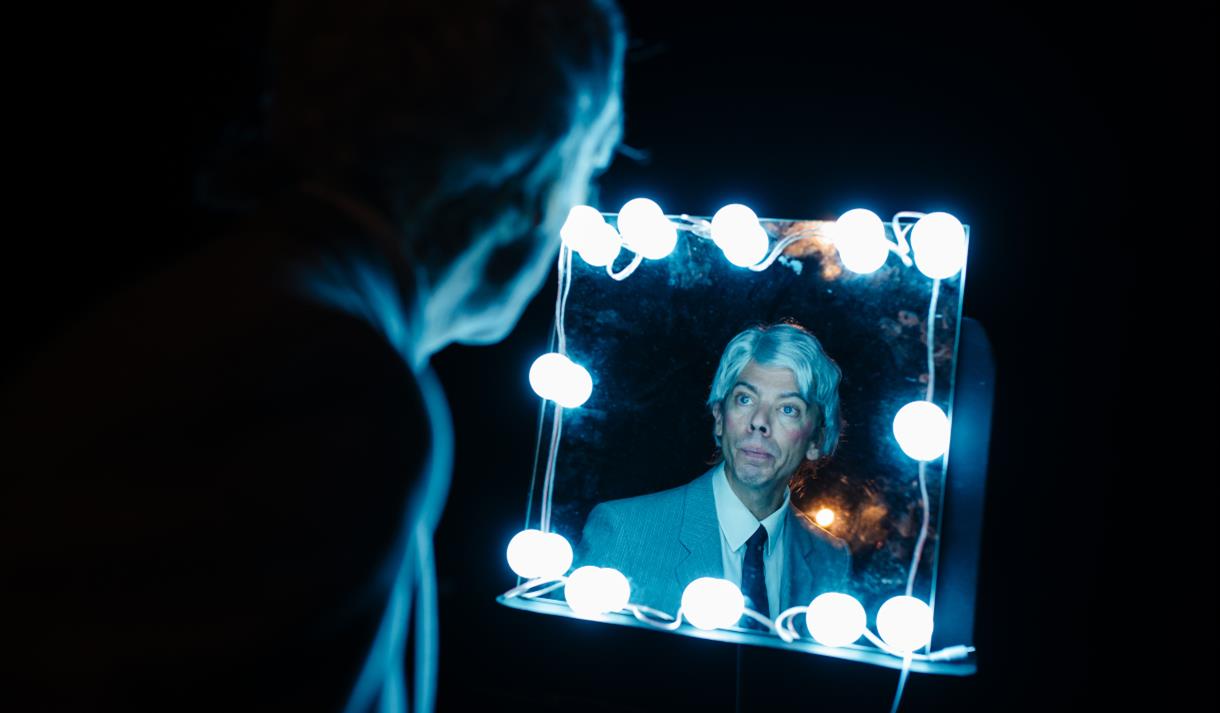 Man in wig looking in dressing room lights in publicity photo for A Shining Intimacy at Theatre Royal Bath