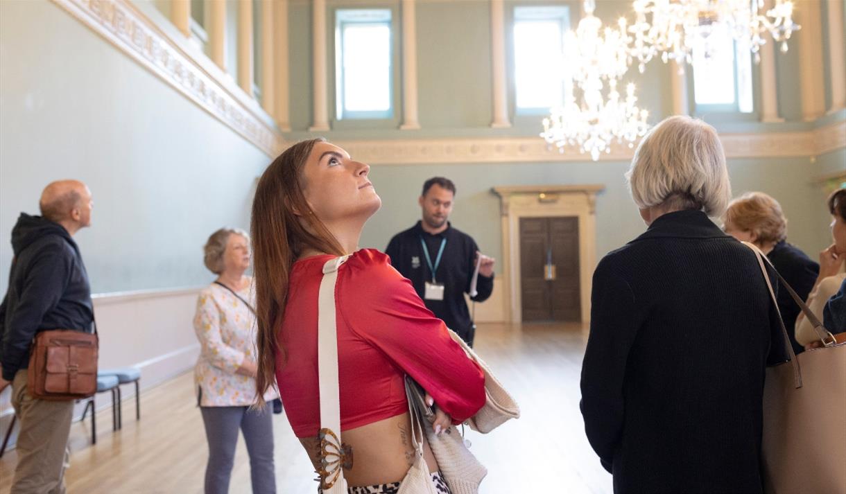 A guided tour group in the Ball Room at Bath Assembly Rooms