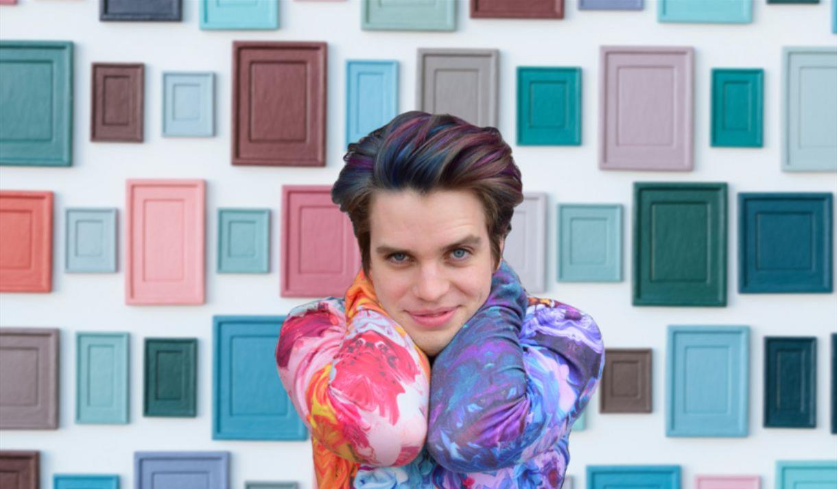 Jim Fishwick in front of a white wall covered in colourful tiles
