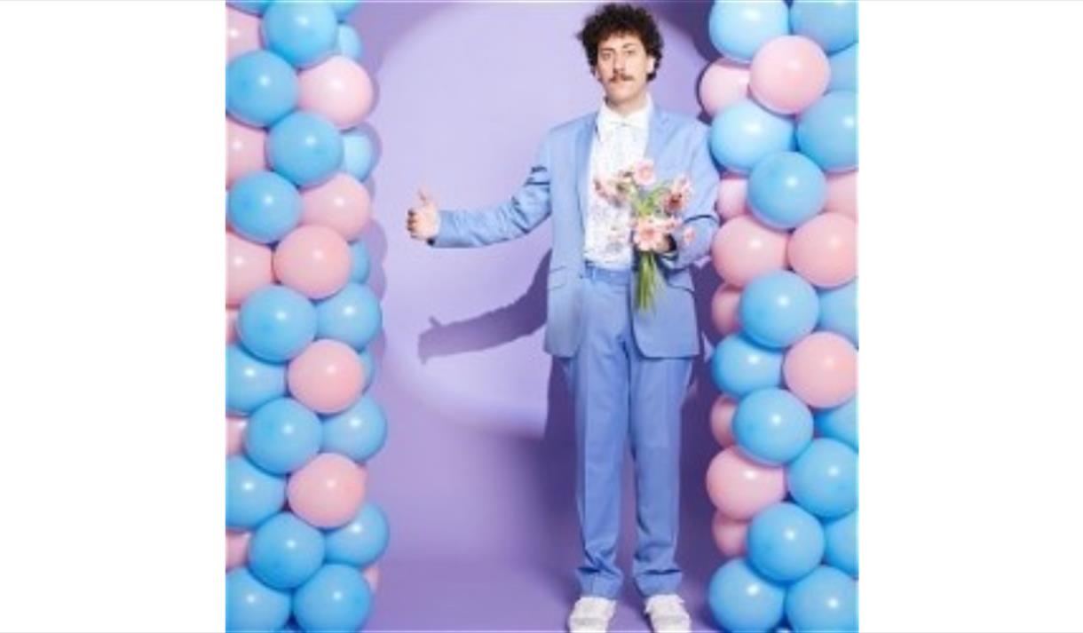 Schalk Bezuidenhout in a purple suit in front of a balloon arch