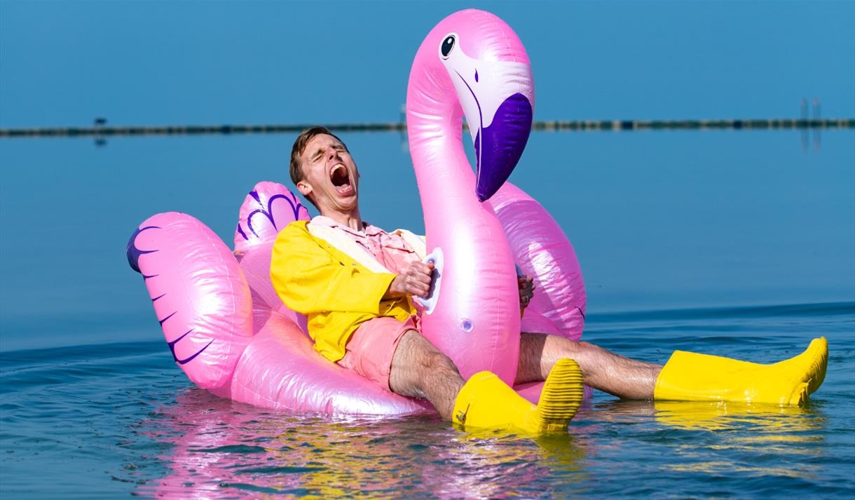 Harry baker sitting on a inflatable pool flamingo.