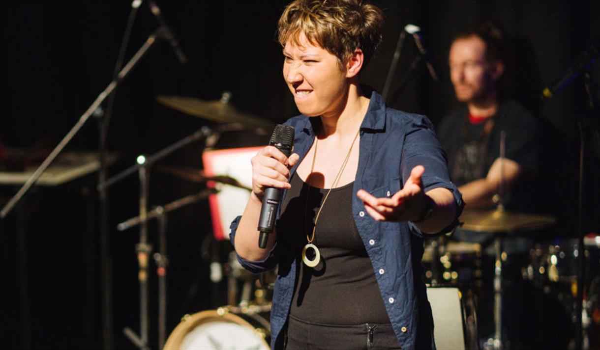 A female wearing a black tank top and blue overshirt performing on stage