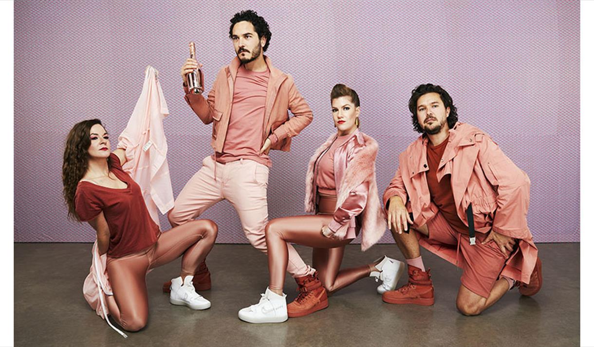 4 peole wearing all pink outfits infront of a purple backdrop