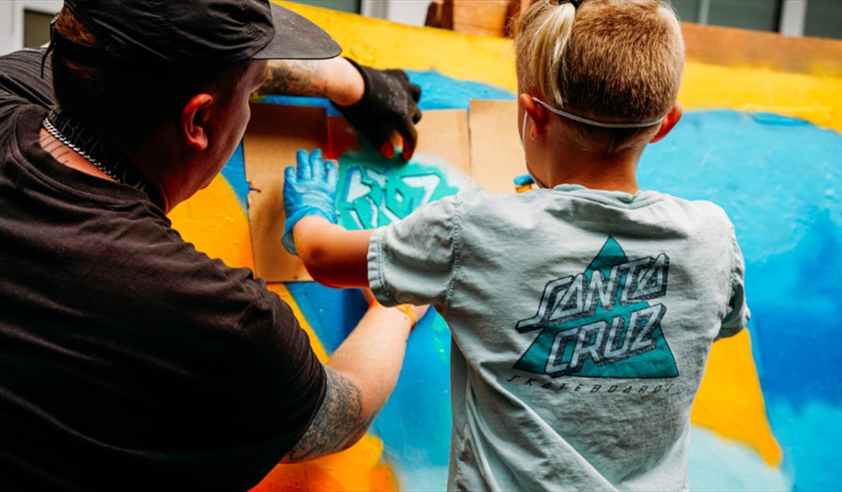 A young child and an adult partaking in a graffiti workshop