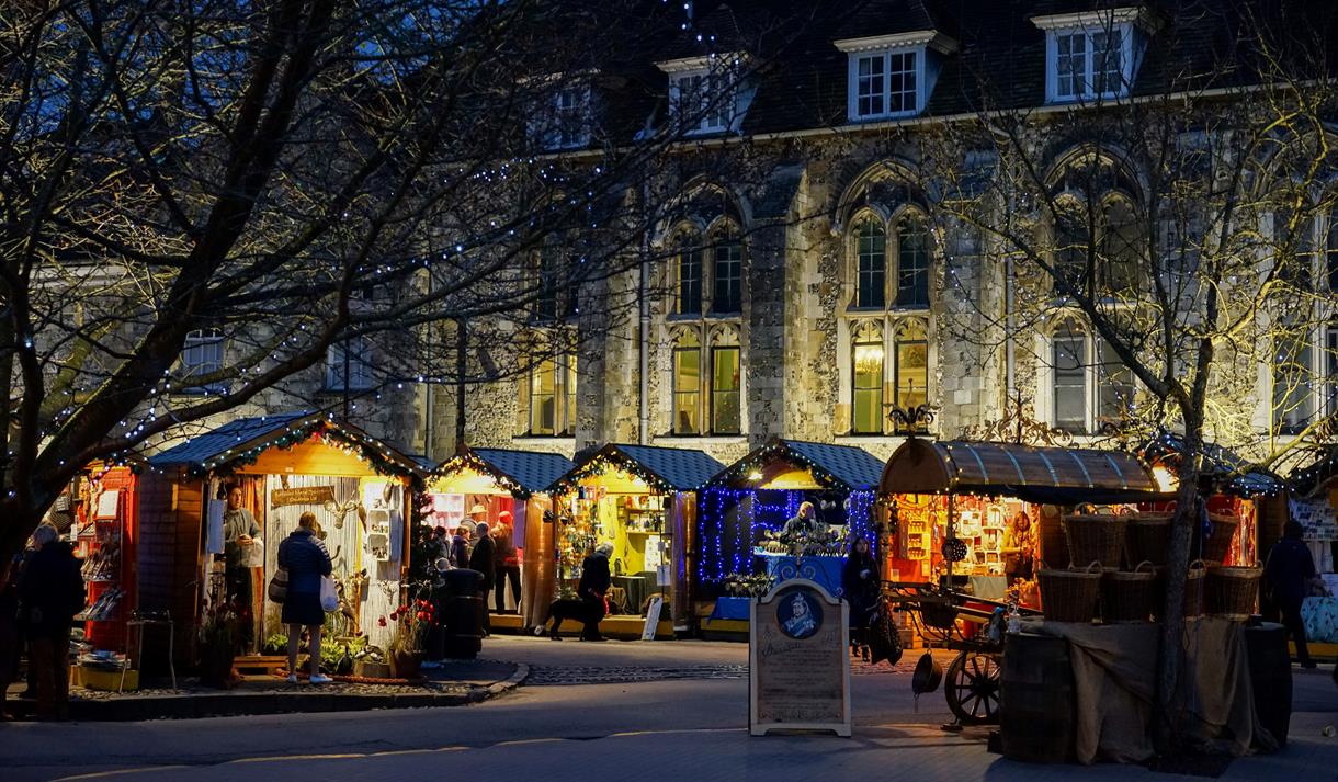 Winchester Cathedral Christmas Market chalets, with Winchester Cathedral in the background at night.