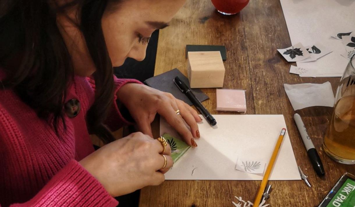 A female wearing a pink jumper carving a stamp