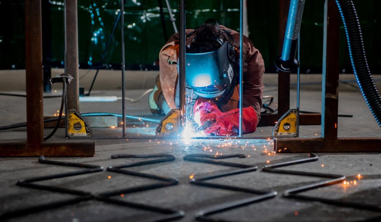 A performer dressed as a welder, welding metal on a stage