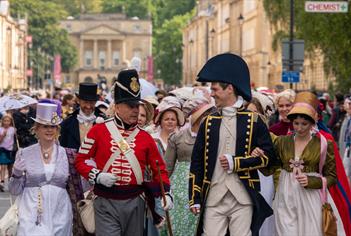 Two men and two women all dressed in Jane Austen-themed costumes leading a procession